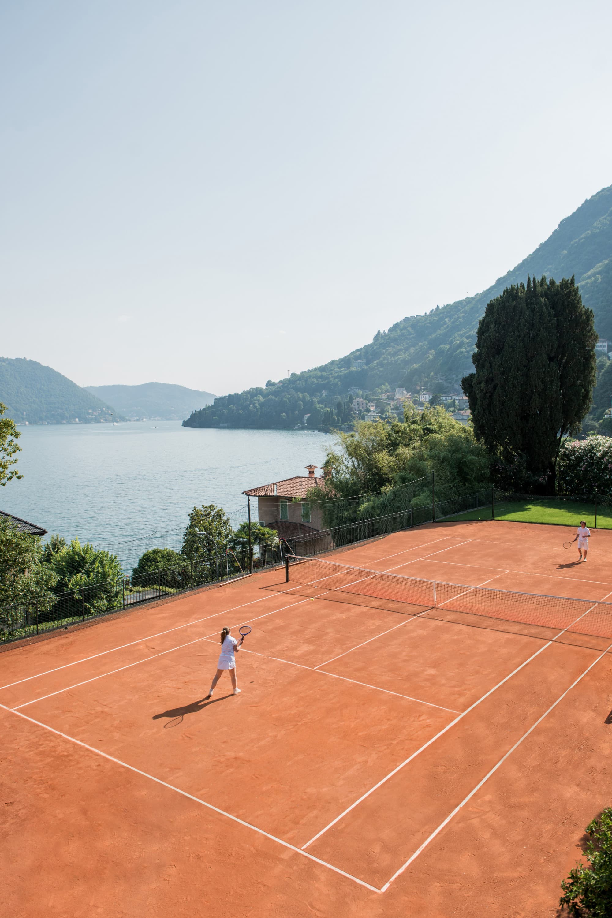 a red-clay tennis court near an alpine lake