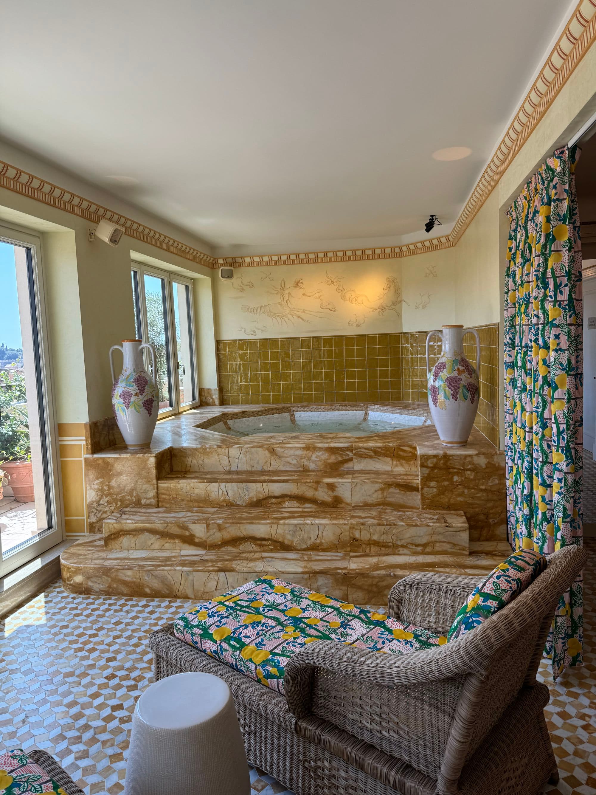 The hotel jacuzzi sits in a marble lounge area next to large windows with sun streaming in from outside.