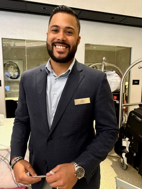Hotel employee in a blue suit smiling to welcome a guest.