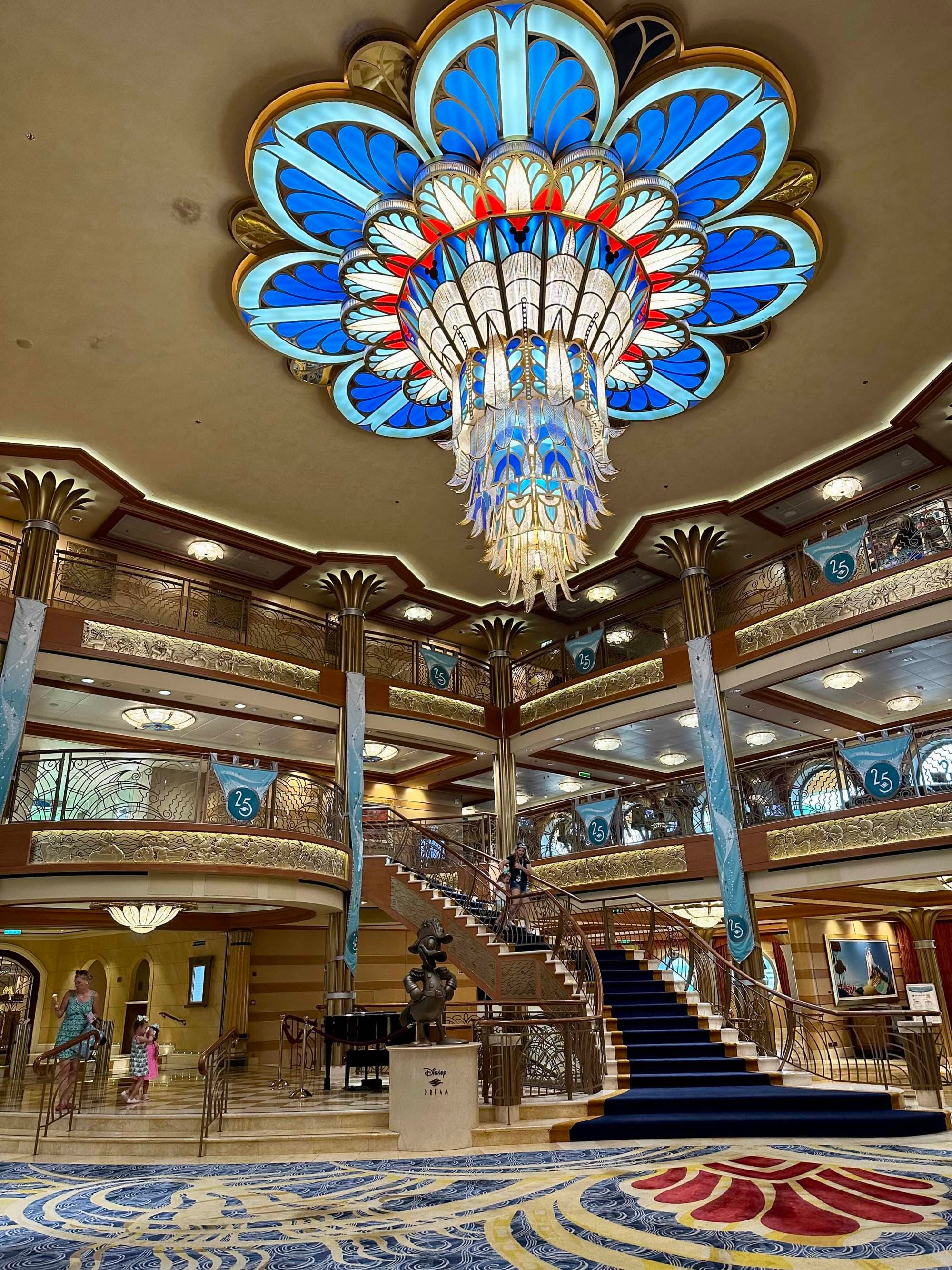 A foyer with a carpeted staircase and an elaborate chandelier of colored glass.