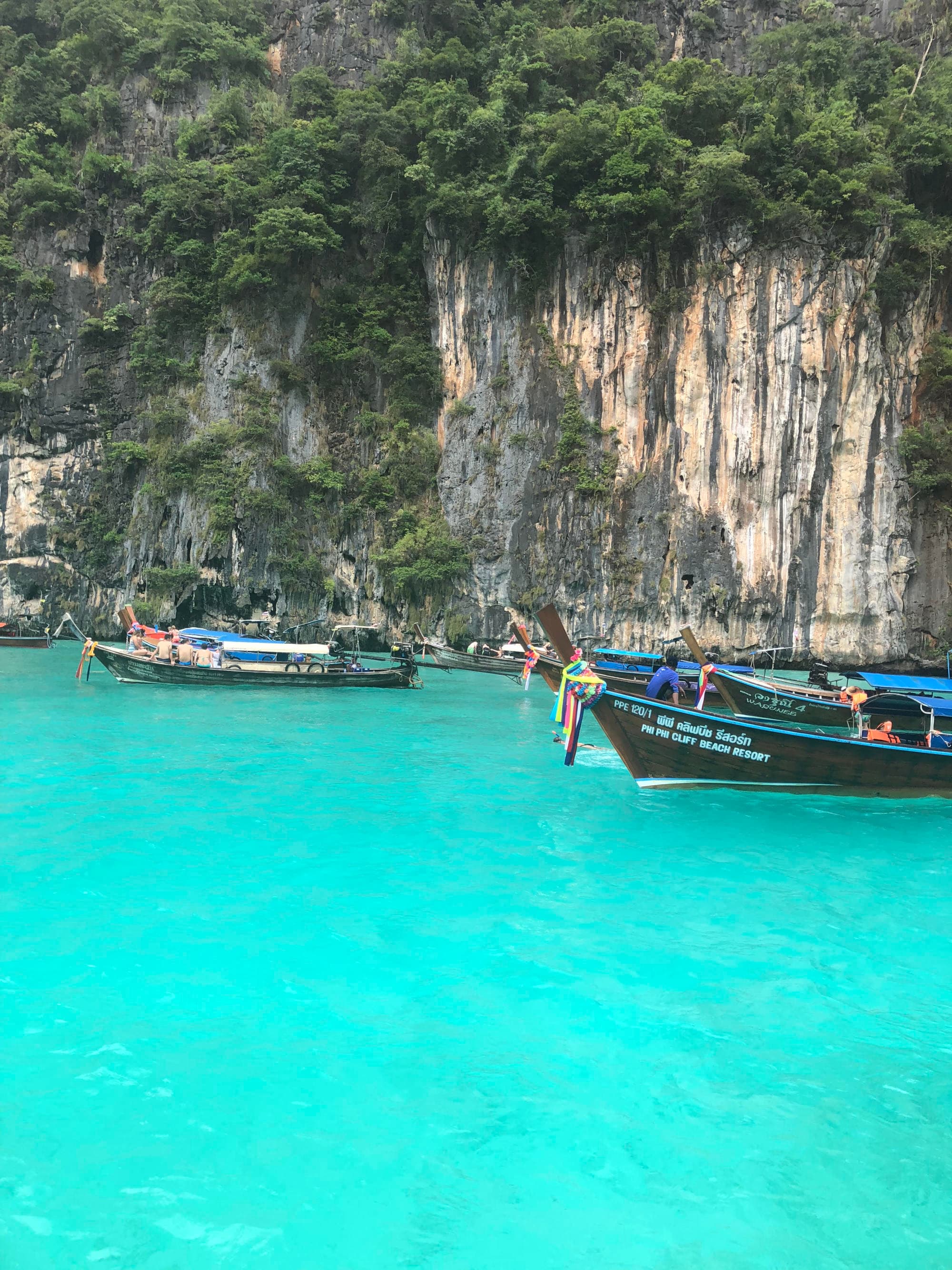 Boats on shallow and bright blue water with steep cliffs in the background.