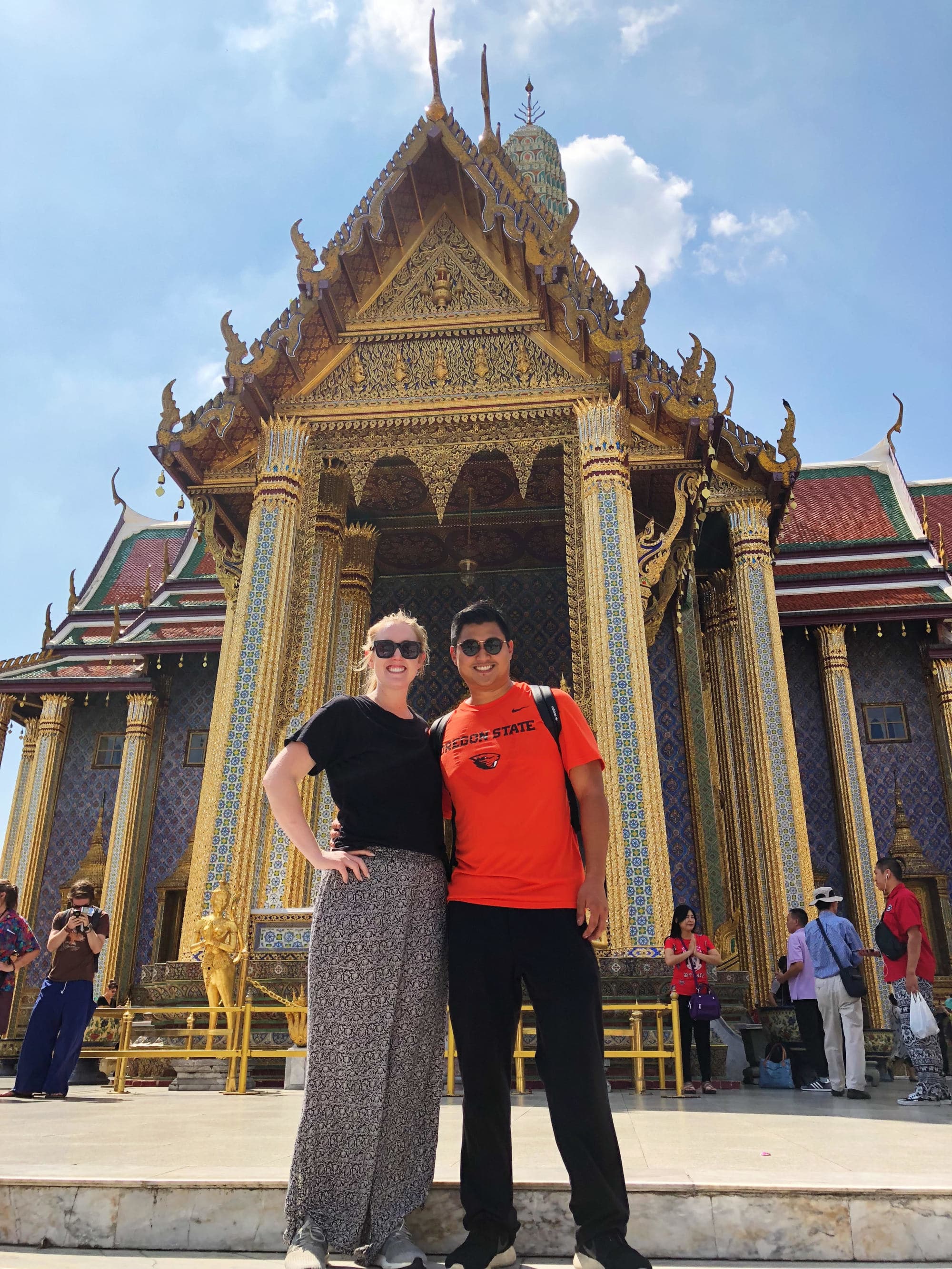 A couple posing in front of a temple with a peaked roof.