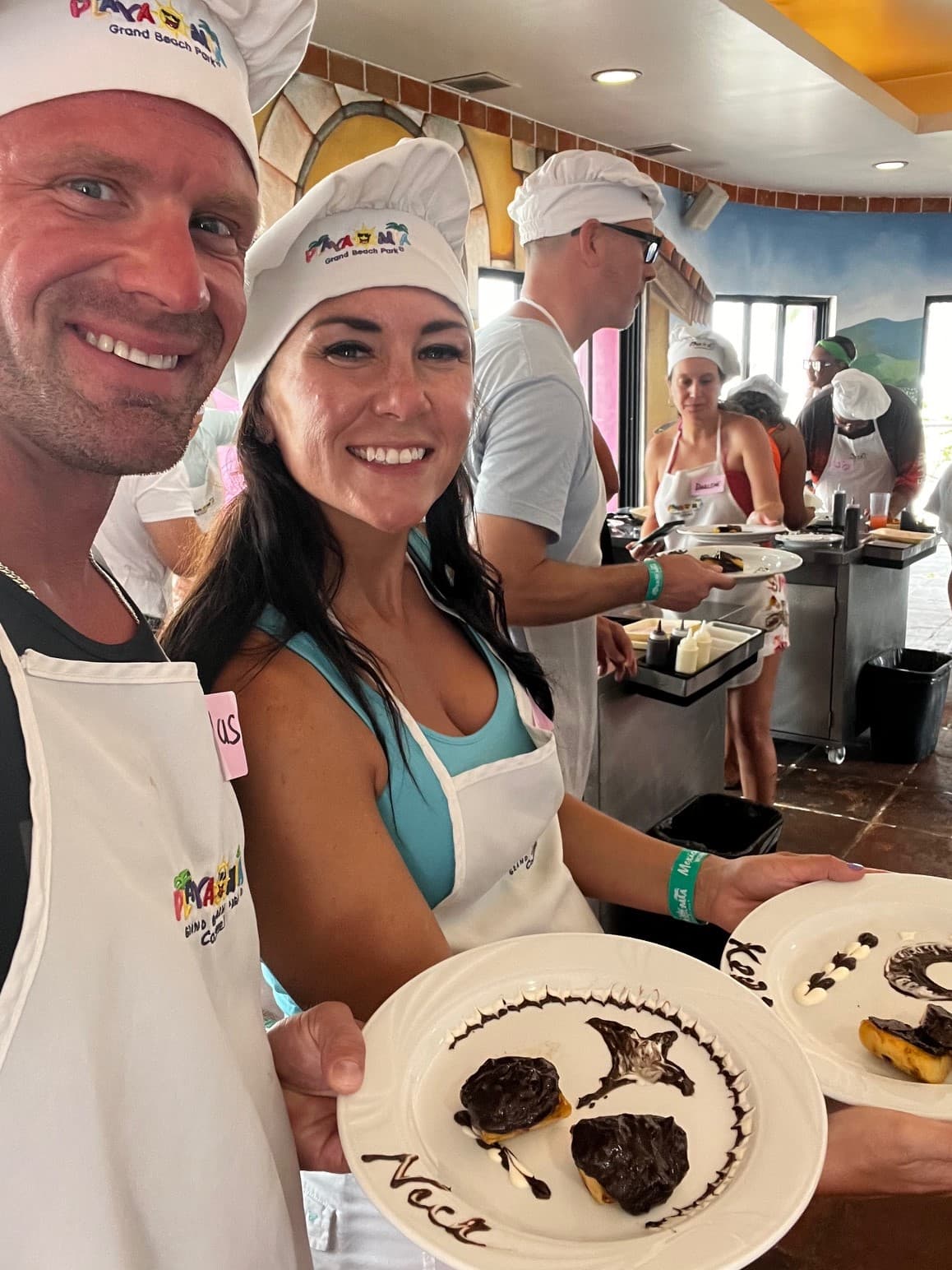 Two people smiling for a photo while holding two white plates of food