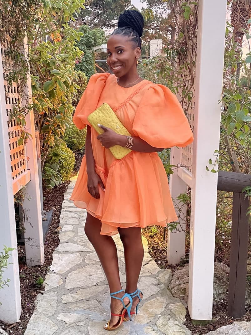 Fora Advisor Fallon Alexandria in orange puff dress and sky blue shoes in garden.