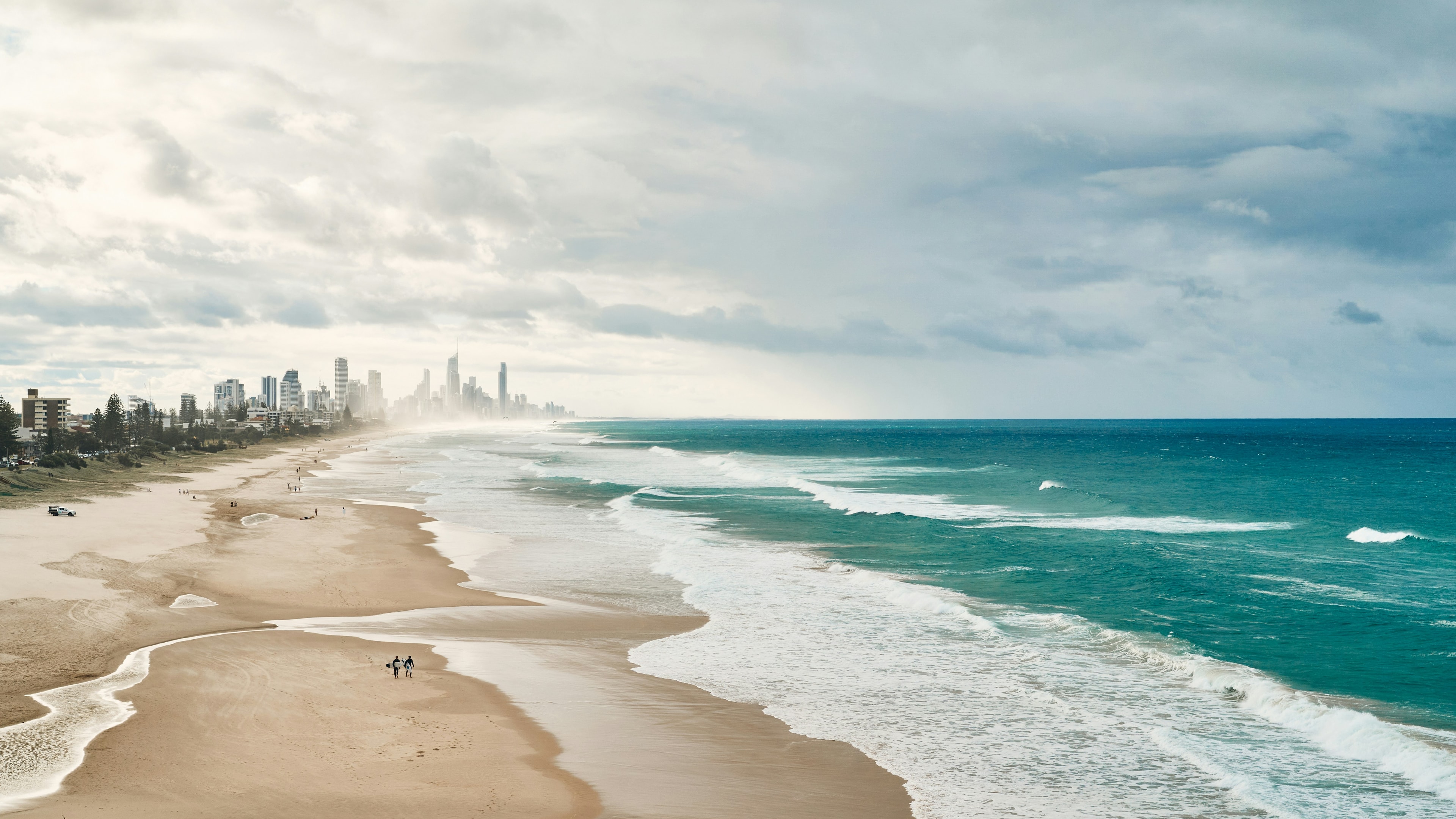 Waves on an expansive beach with high rise buildings in the background.