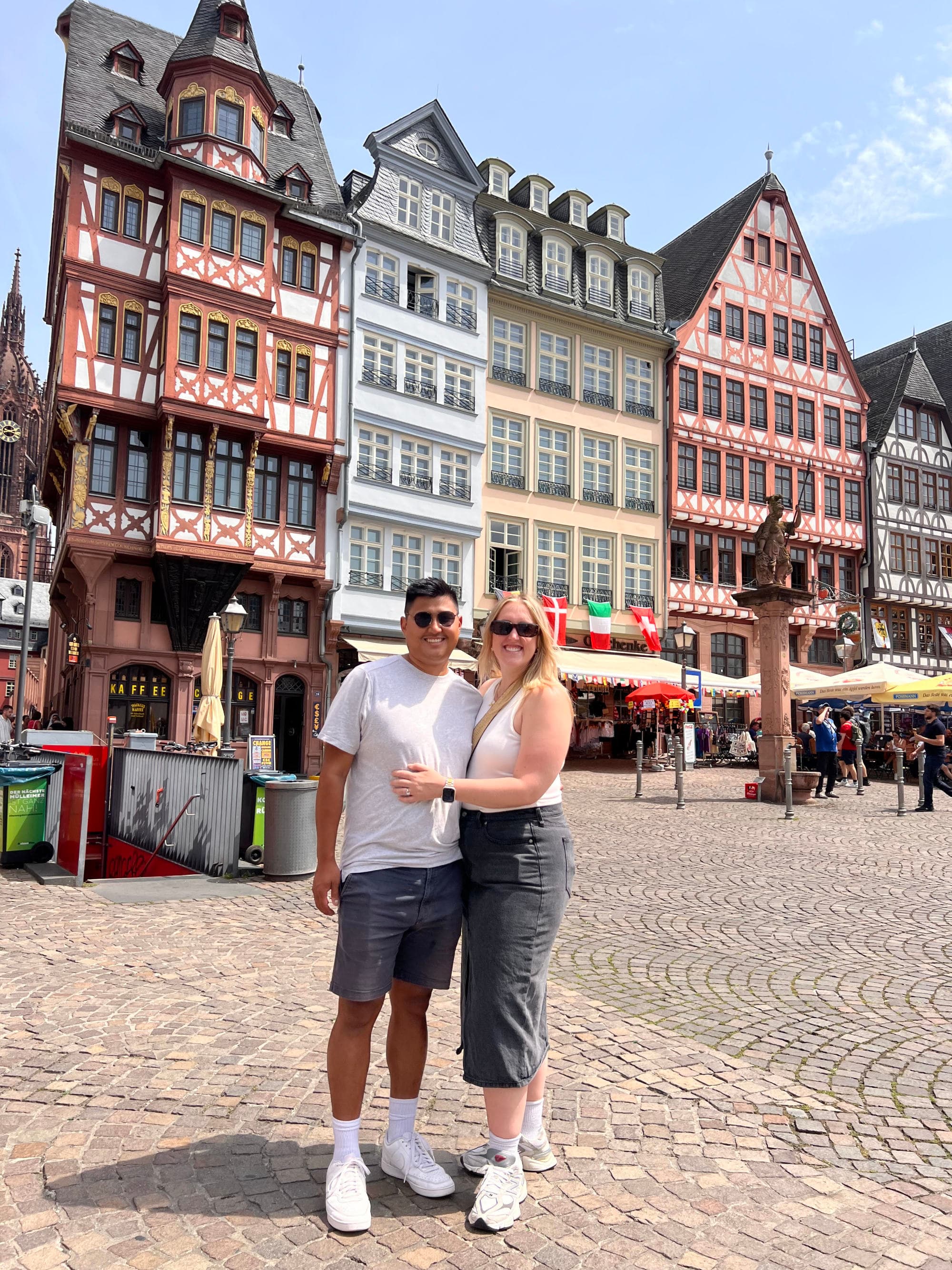 A couple posing for a photograph outside on a city street in front of colorful tall buildings