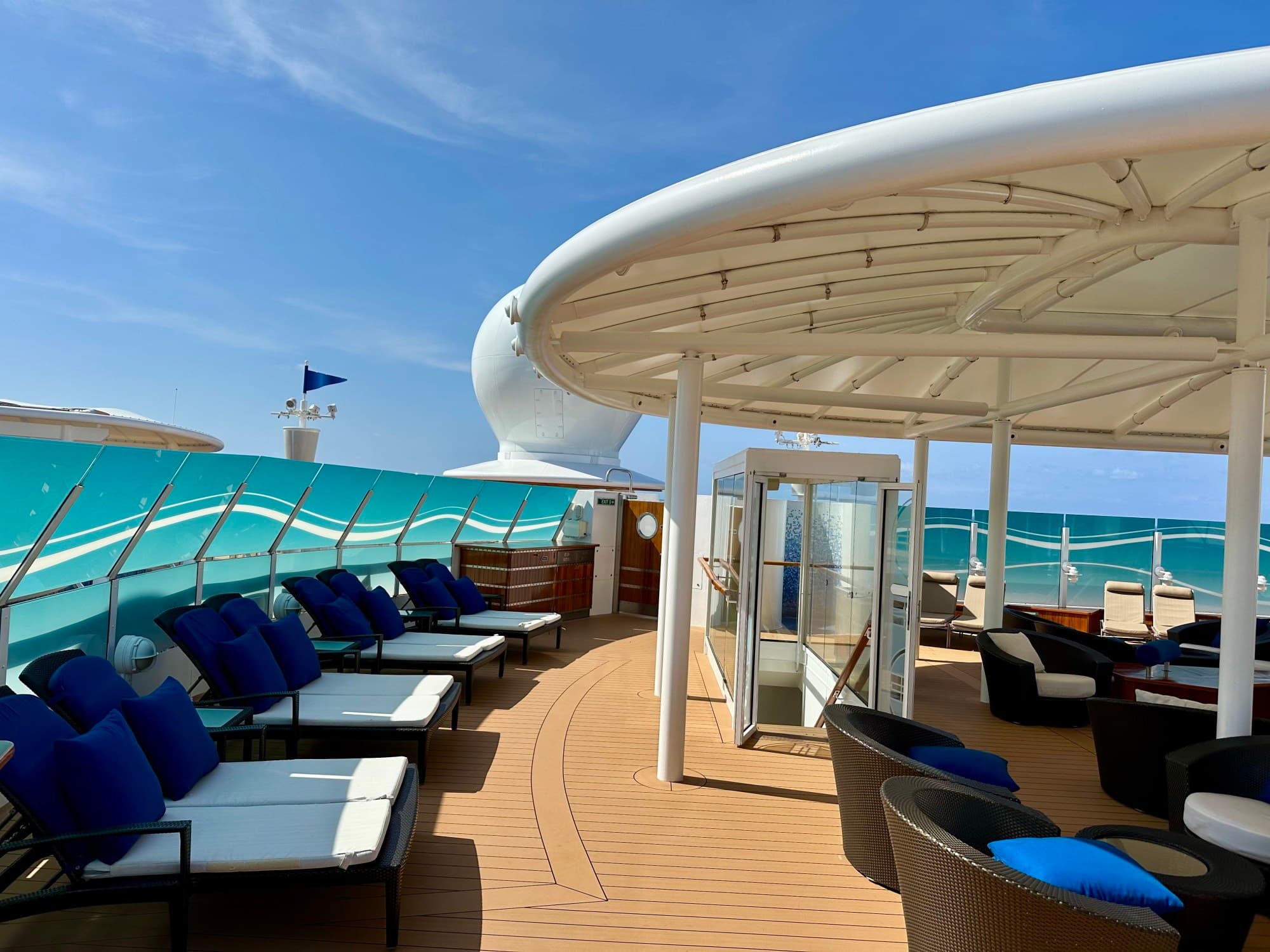 Covered open-air deck on a cruise ship with blue- and white-uphostered chairs.