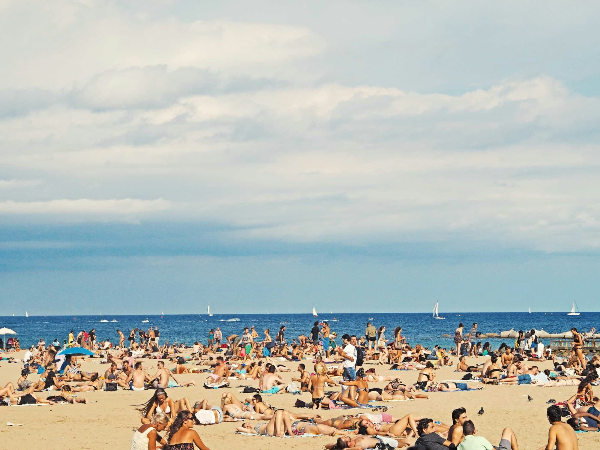 A seaside view of the beach filled with visitors on a cloudy day.