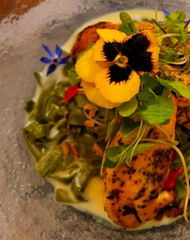 Plate of food with yellow sauce and edile flowers.