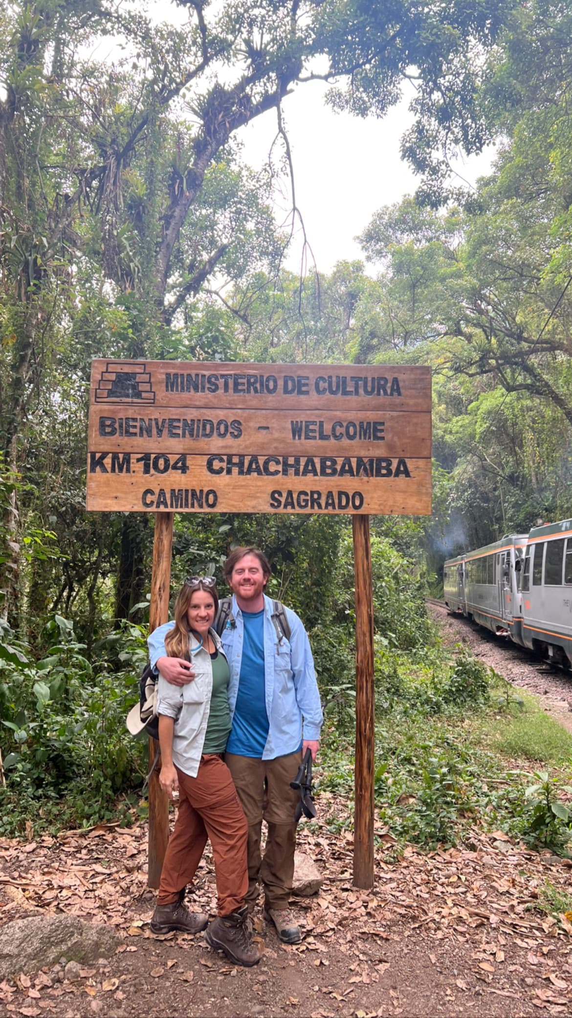 Couple poses in front of a sign in the jungle.