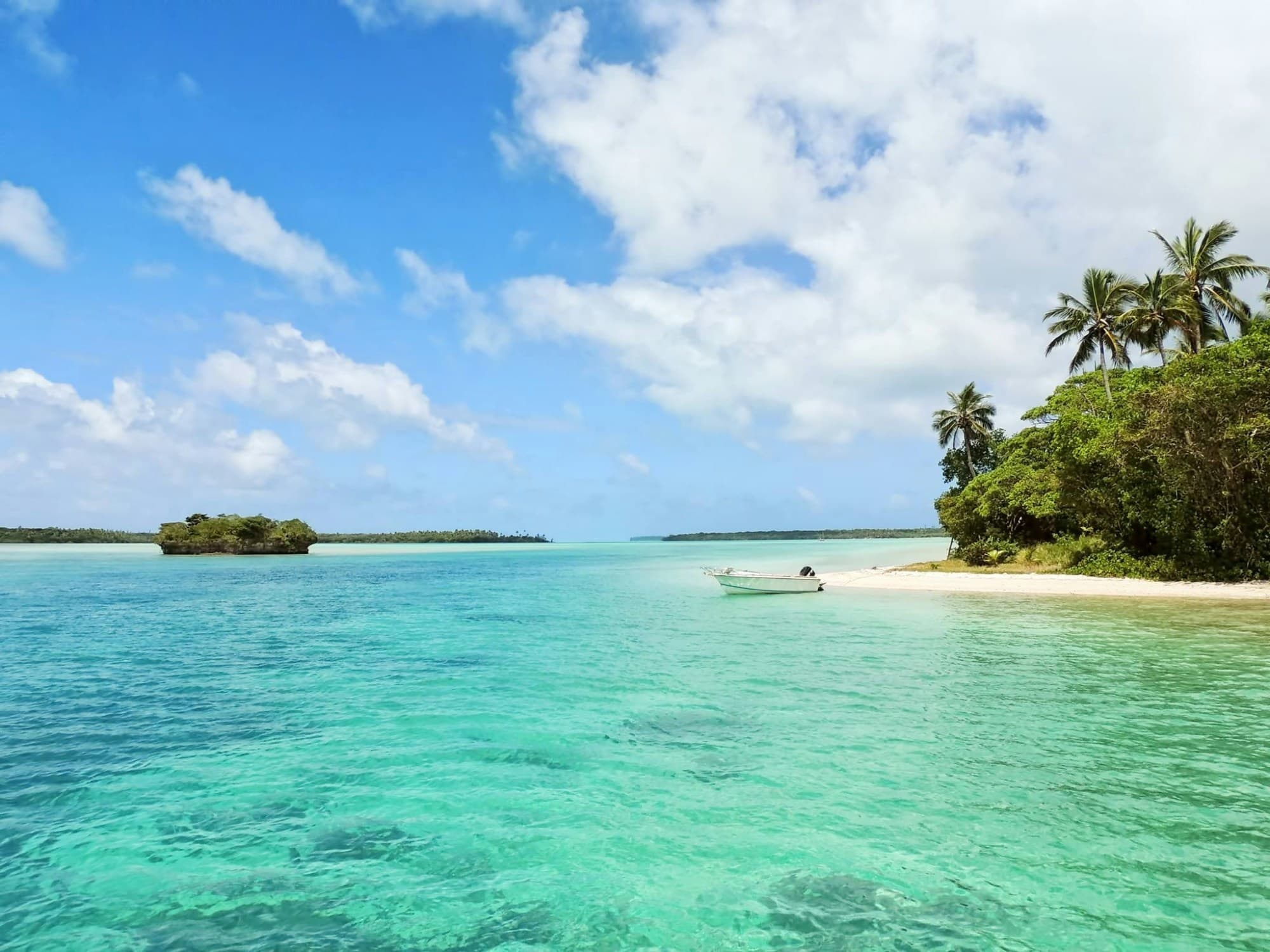 A view of the clear, azure sea, with a small boat, and shores full of natural greenery.
