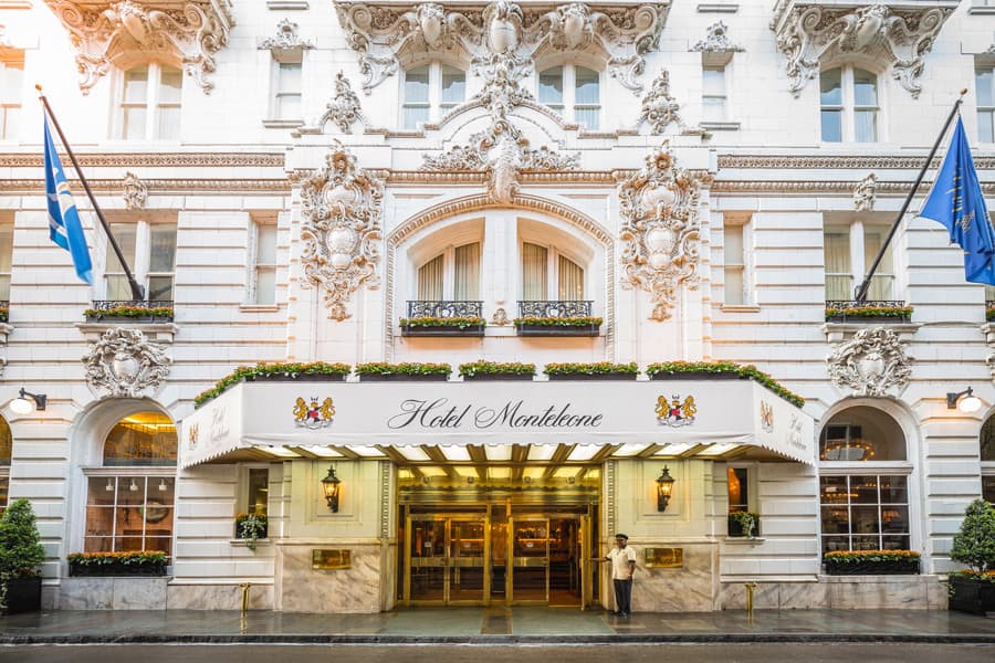 The grand exterior of the Monteleone Hotel, New Orleans, with elaborate stone work, blue flags, sconces, french windows and a gold door.