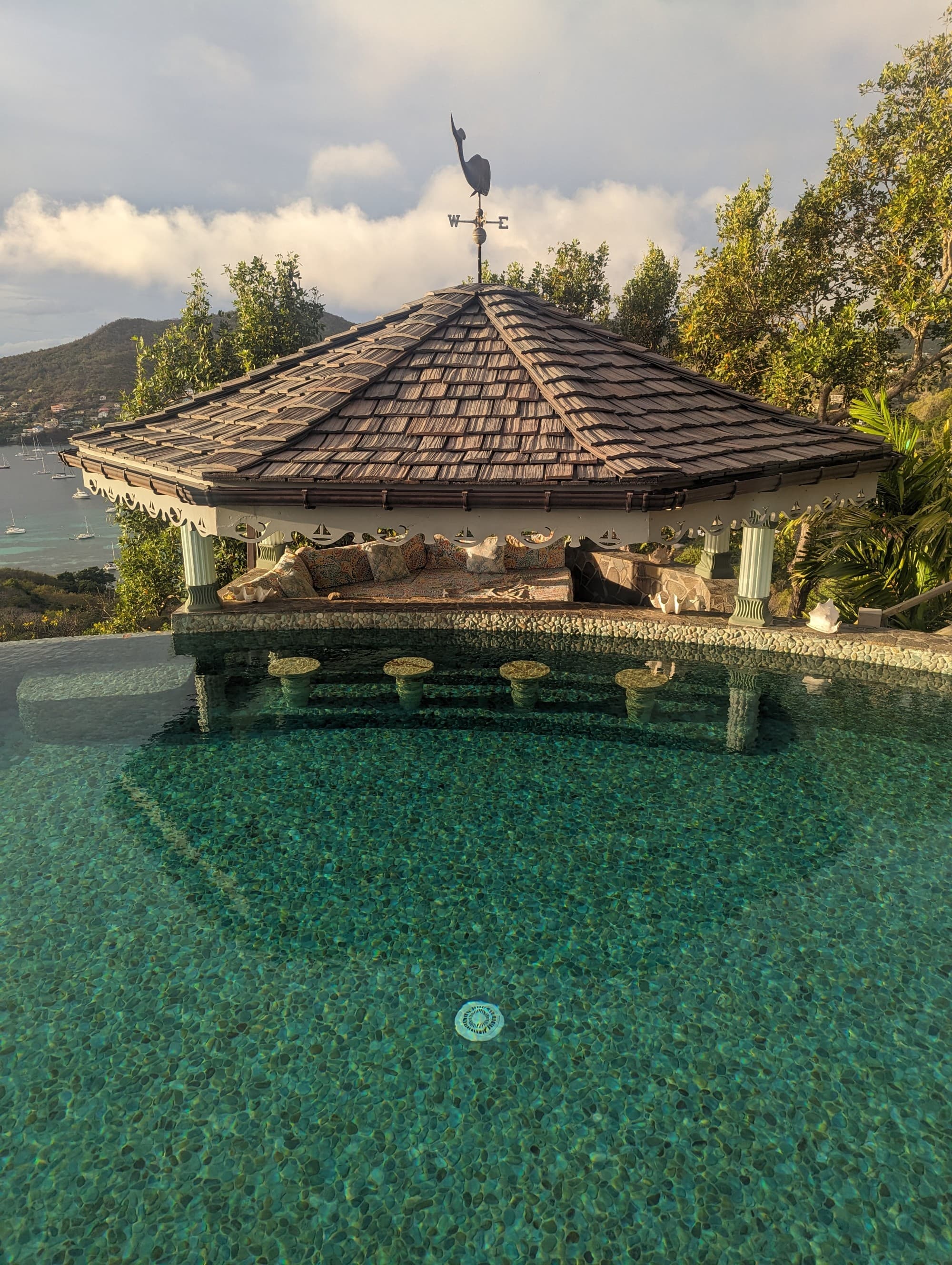 A pool with a seaside hut next to it and a view of the sea and mountains in the distance.