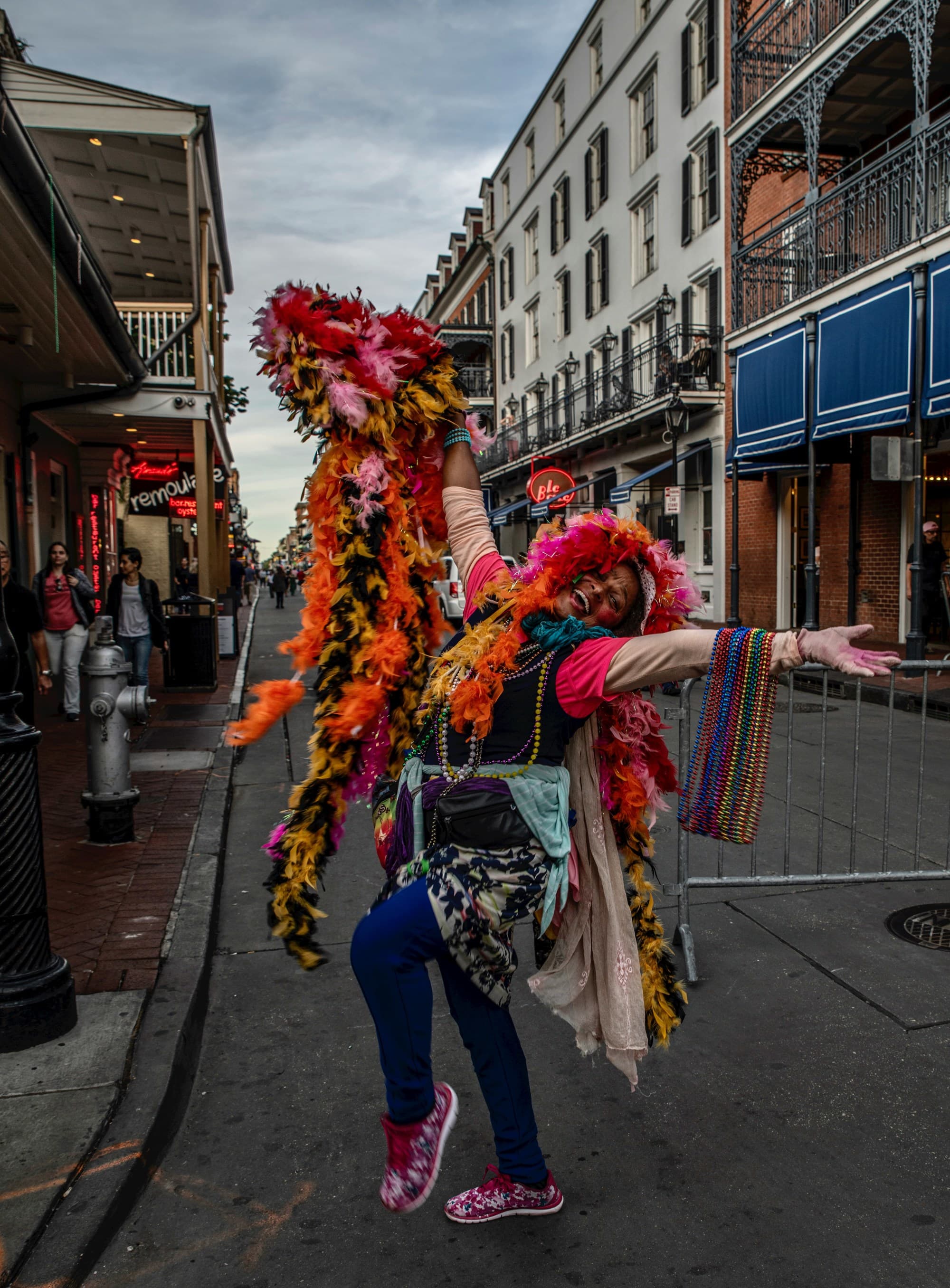 A woman adorned in flowers with her hands spread open posing in front of buildings outside in New Orleans.