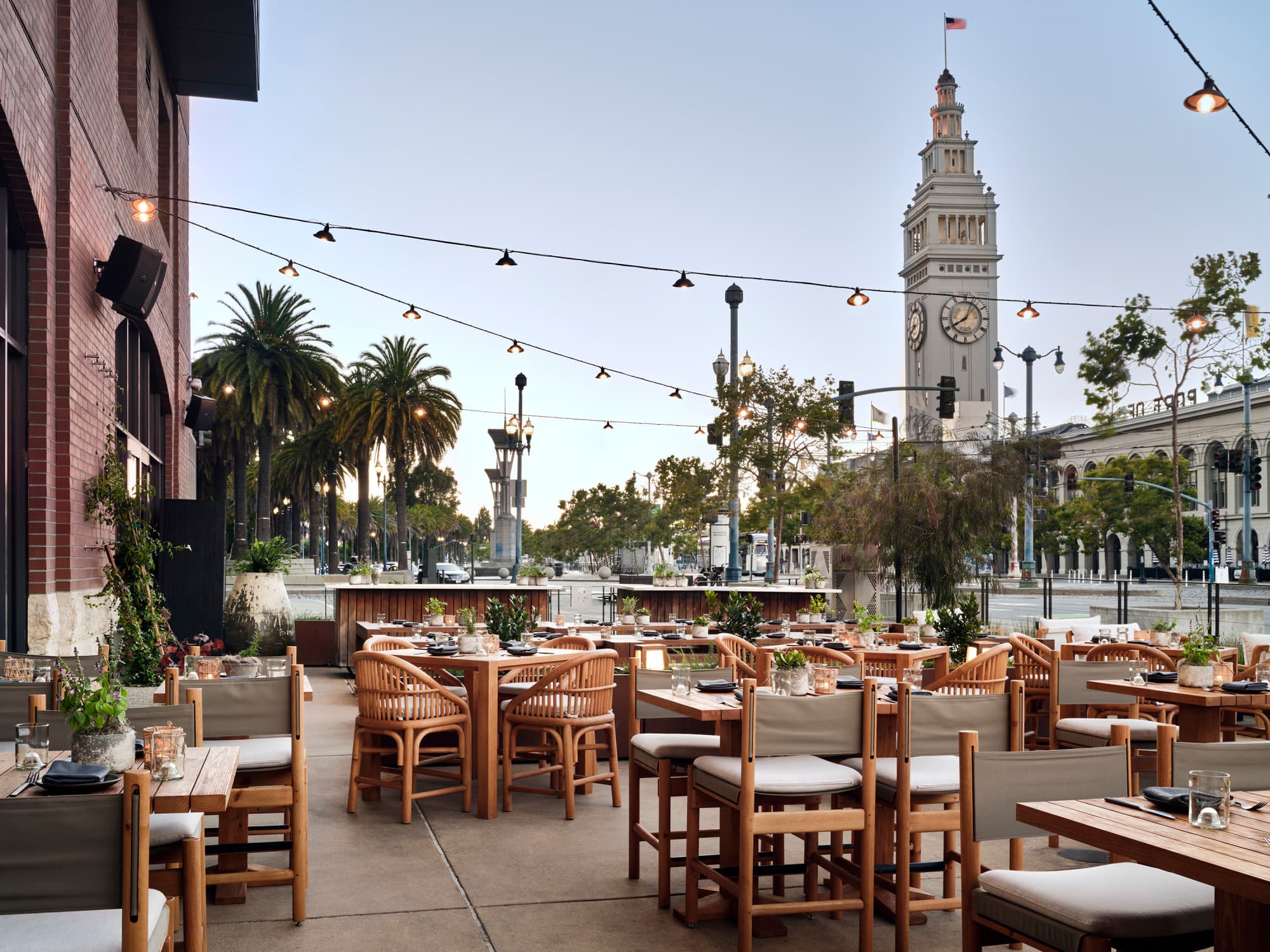 1 Hotel SF with wooden chairs and tables, string lights and a clock tower.