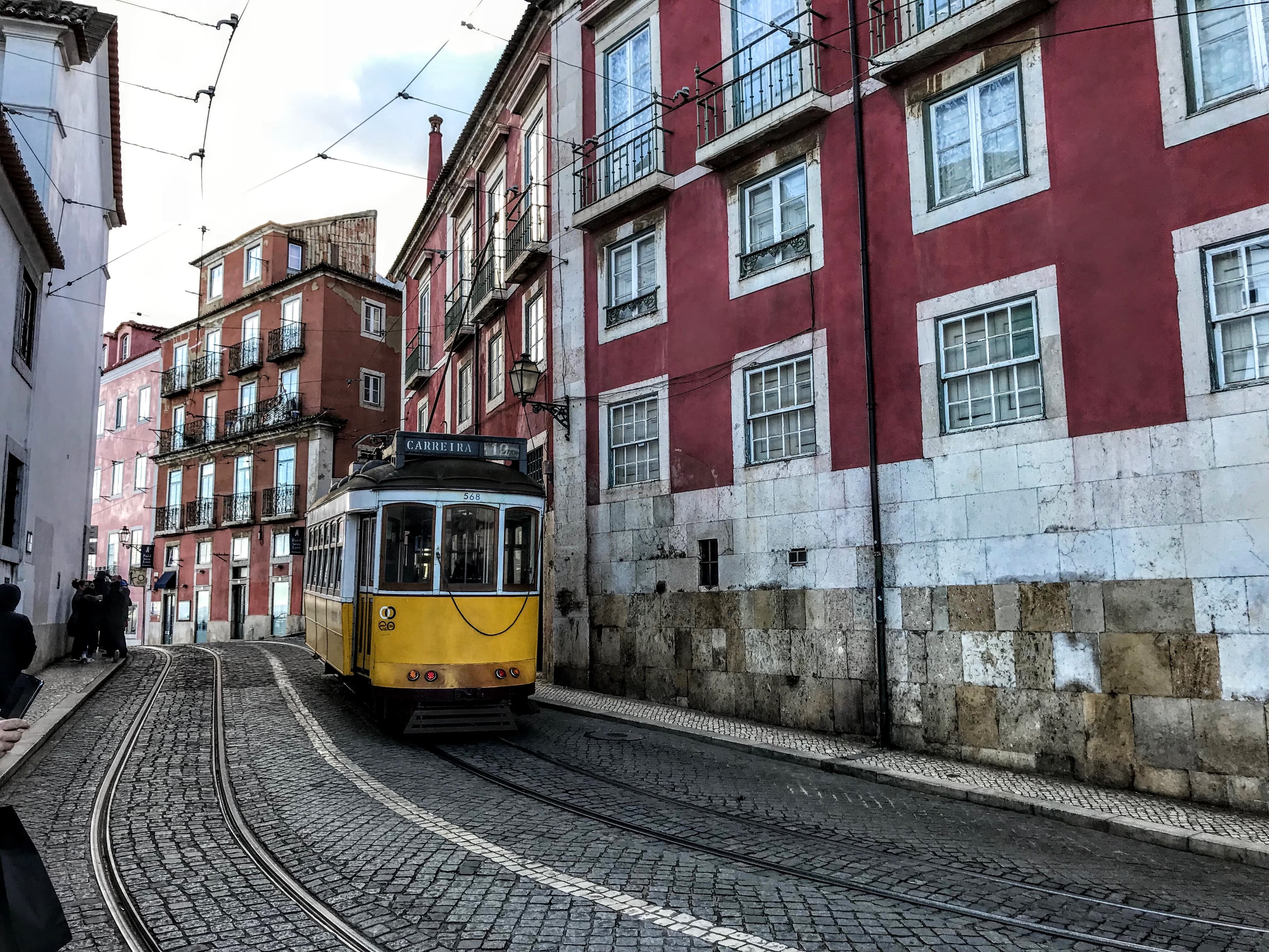 View of a yellow trolley coming down the track besides a red building in Lisbon