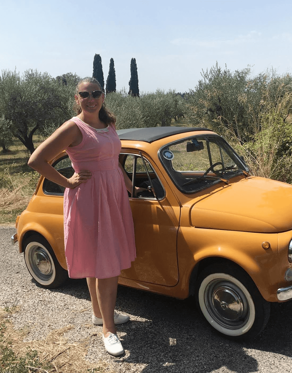 Kathryn wearing a pink dress and posing in front of a yellow car outside.