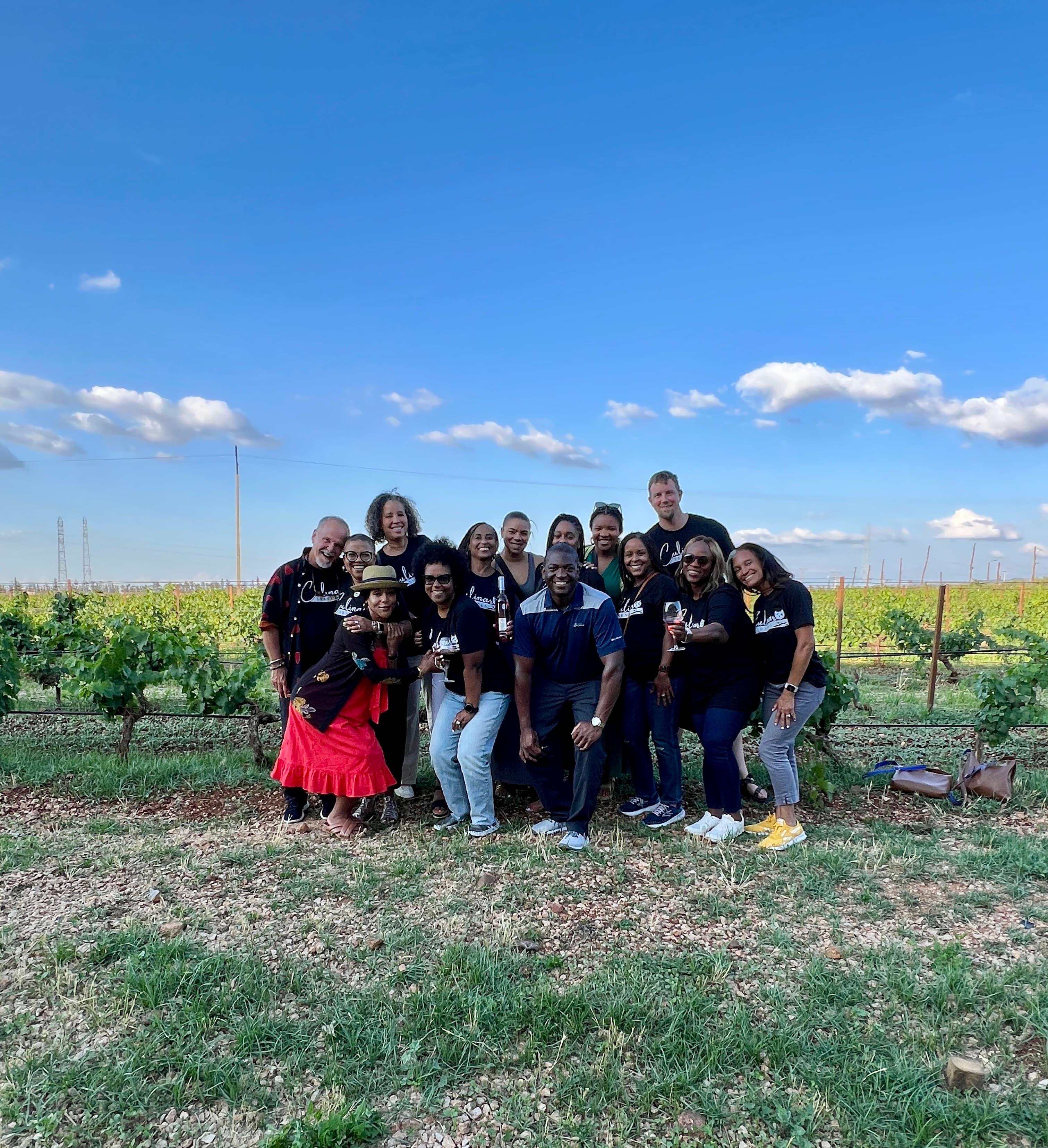A group of people posing for a photo outside while standing on grass with bushes in the background.
