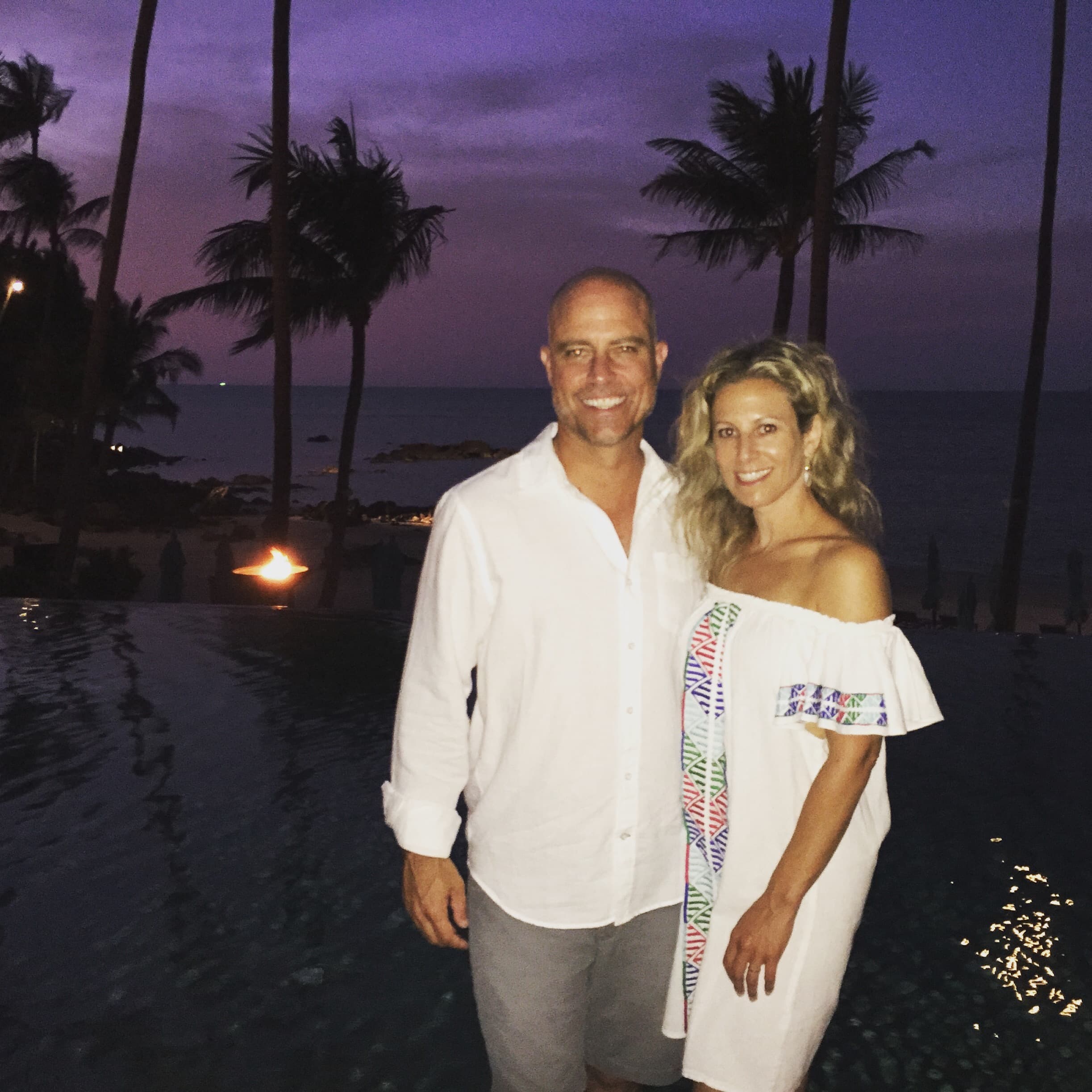 Sara wearing a white dress standing with a man in front of a beach at dusk